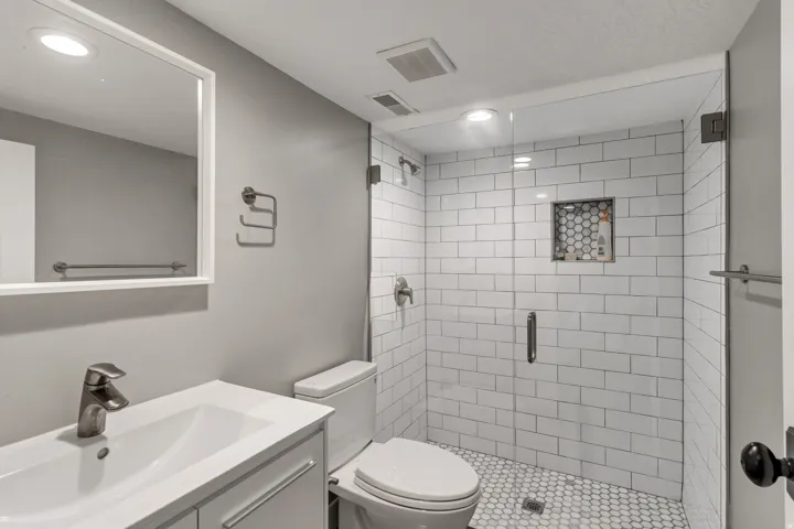 Bathroom featuring a glass-enclosed shower with white subway tile, a hexagonal tile shower niche, and a white hexagonal tile floor