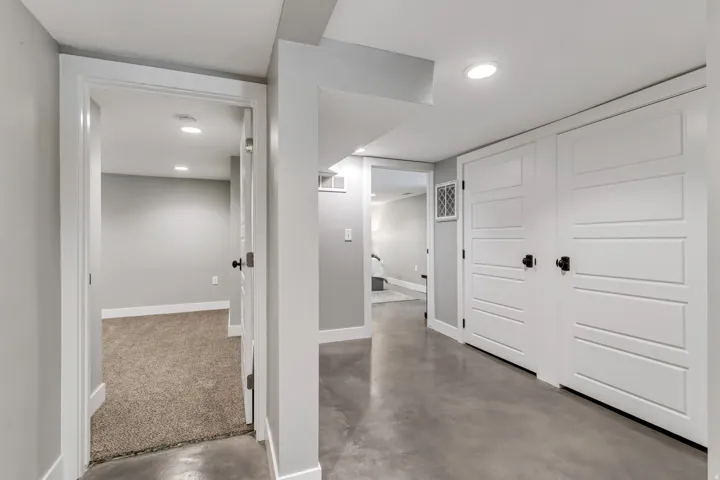 Hallway featuring concrete flooring, recessed lighting, white trim, and multiple white panel doors with black hardware