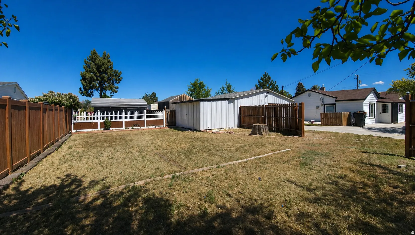 Expansive backyard space featuring a wood fence, a white storage shed, and a section of white picket fencing