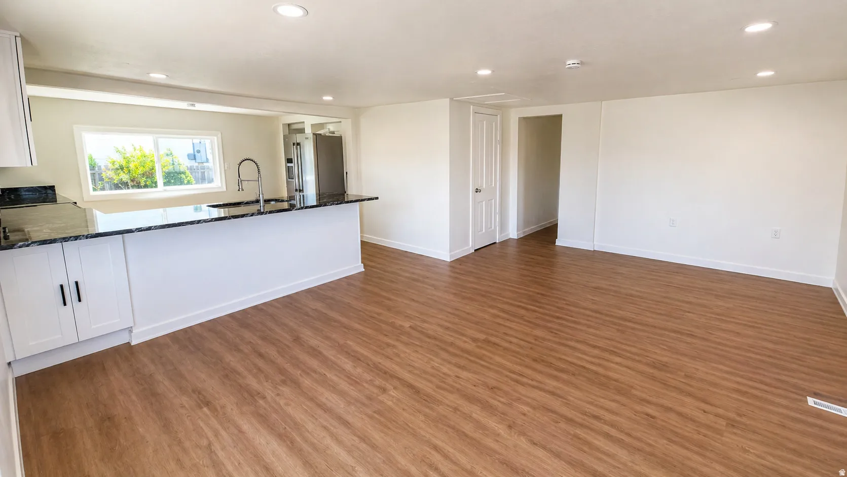 Open-concept living space featuring wood-finish flooring, recessed lighting, and a kitchen with white cabinetry, dark countertops, and a modern gooseneck faucet
