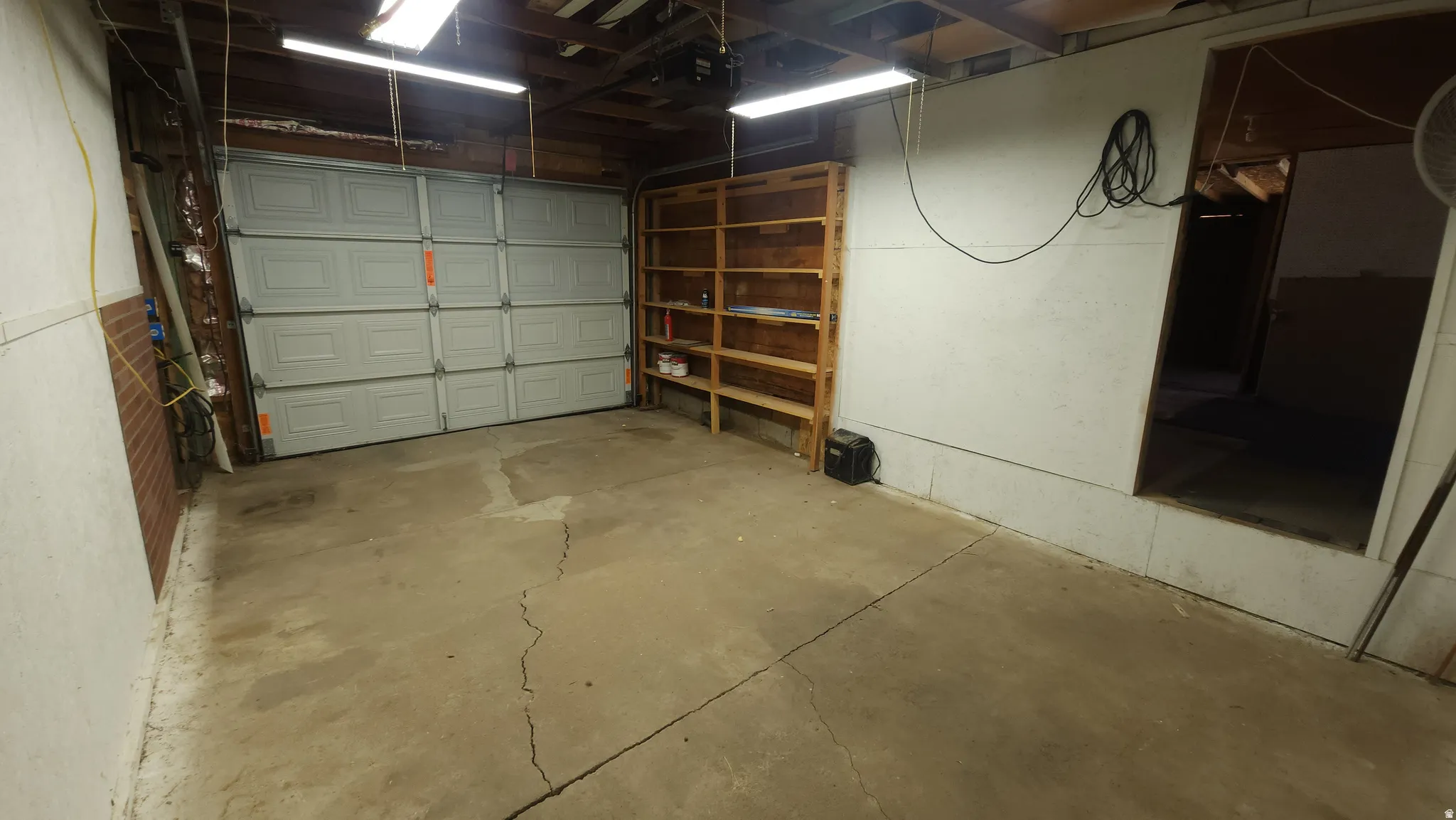 Attached garage featuring a concrete floor, a paneled garage door, exposed ceiling joists, and a built-in wooden shelving unit