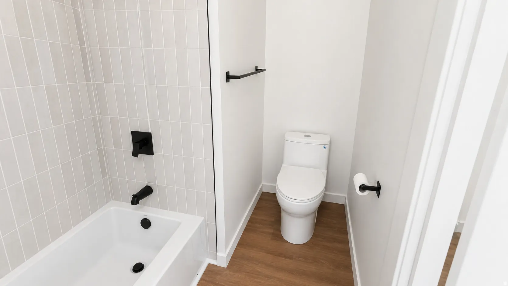 Bathroom featuring a white bathtub, light grey vertical subway tile surround, matte black fixtures, and wood-finish flooring