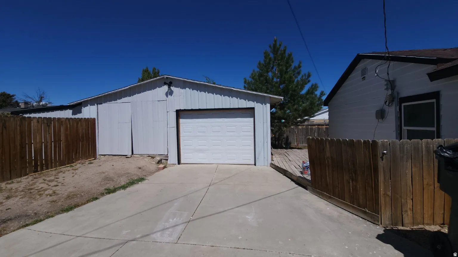 Detached garage with a white overhead door, concrete driveway, wood privacy fencing, and an adjacent wood deck