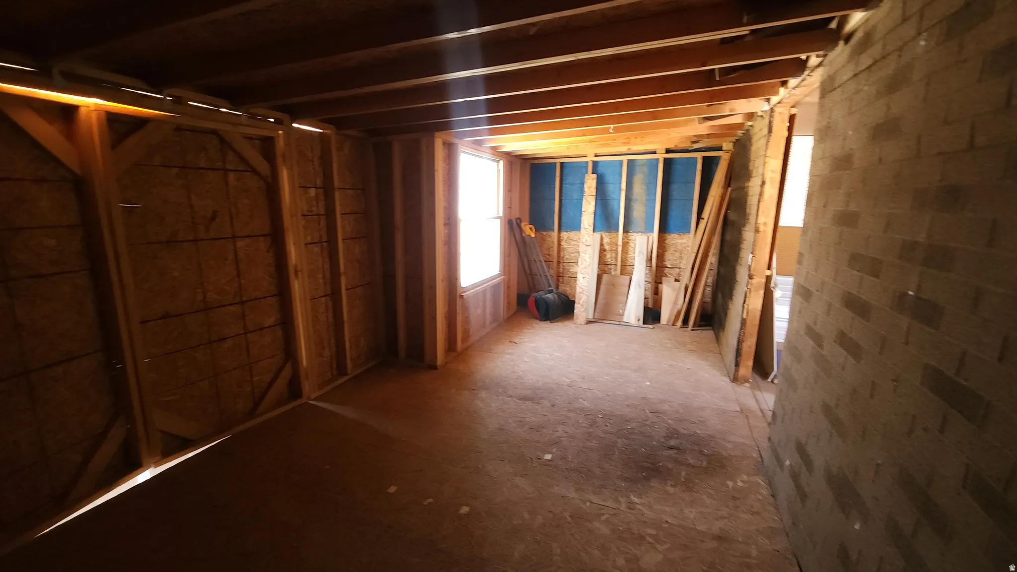 Unfinished interior space featuring exposed wood framing, plywood walls, and an exposed brick wall