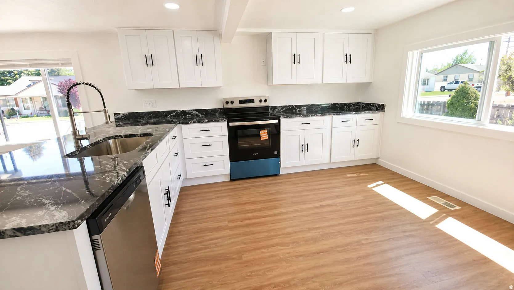 Kitchen featuring white cabinetry with dark hardware, dark patterned countertops, stainless steel appliances, wood-finish flooring, and a large window