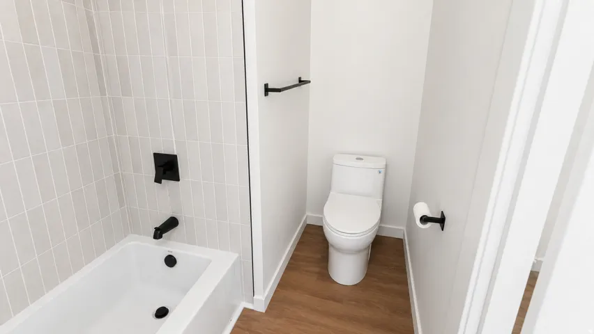 Bathroom featuring a white bathtub, light grey vertical subway tile surround, matte black fixtures, and wood-finish flooring