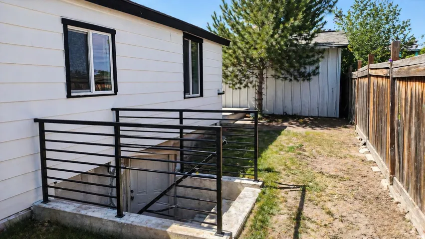 Exterior wall with white siding, black trim windows, and a basement entry featuring black metal railings