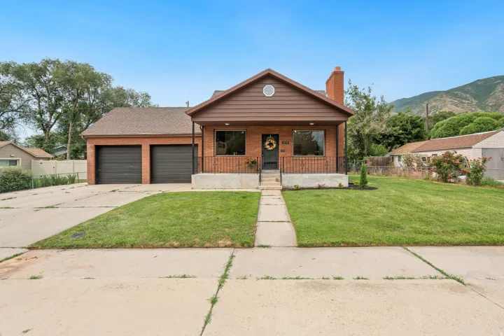 Brick exterior residence featuring a two-car garage, front porch with wrought iron railing, and a manicured lawn