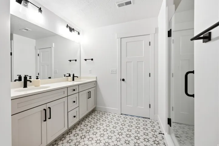 Dual sink vanity featuring light gray cabinetry with matte black hardware, white countertops, and black wall-mounted faucets