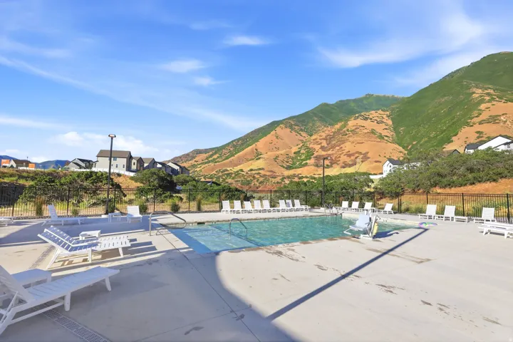 Community swimming pool with surrounding concrete deck, multiple lounge chairs, and a mountain backdrop