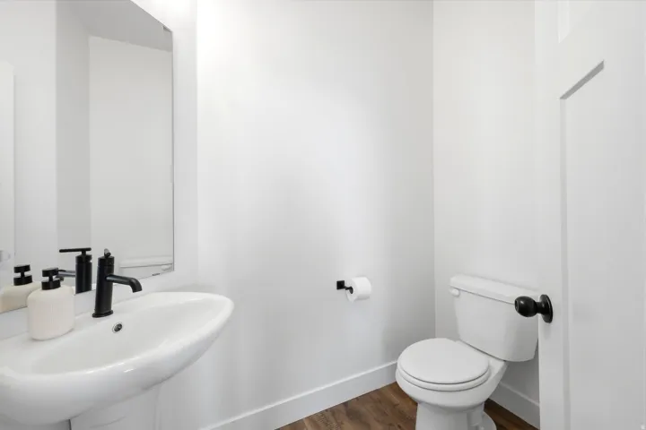 Bathroom featuring a pedestal sink with a matte black faucet, a toilet with a matte black handle, and wood-finish flooring