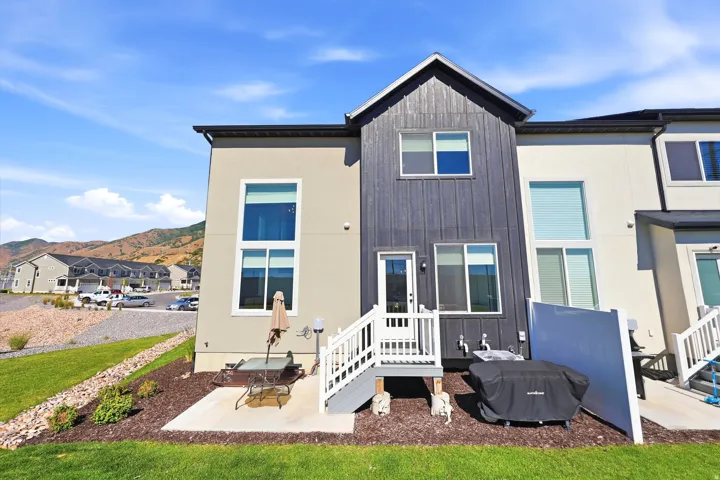 Rear exterior featuring a concrete patio, wooden deck with white railings, and a two-story design with a mix of stucco and vertical plank siding