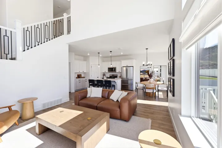 Open concept living space featuring vaulted ceilings, wood-finish flooring, a contemporary staircase with black metal balusters, a kitchen with white cabinetry and stainless steel appliances, and a dining area with modern lighting