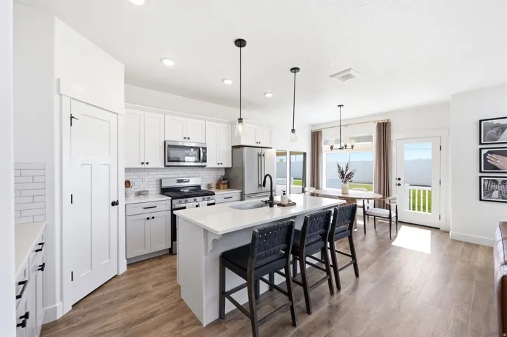 Open-concept kitchen featuring white shaker cabinetry, stainless steel appliances, a subway tile backsplash, and a large island with a countertop