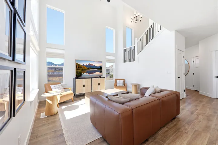 Vaulted living area featuring wood-finish flooring, a contemporary black metal staircase railing, and multiple tall windows