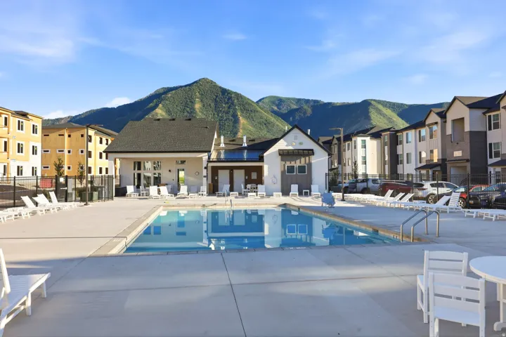 Expansive outdoor pool area with surrounding concrete decking, flanked by modern multi-story residential buildings and a clubhouse structure, all set against a prominent mountain backdrop