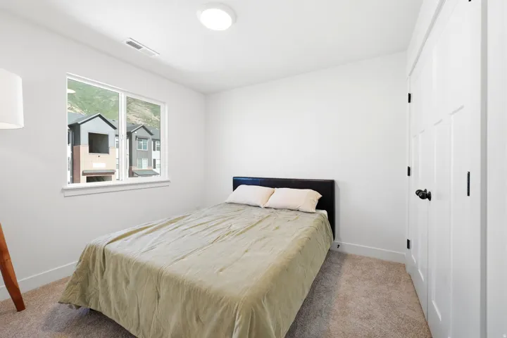 Bright bedroom featuring a large window, neutral carpeting, and a white paneled door with matte black hardware