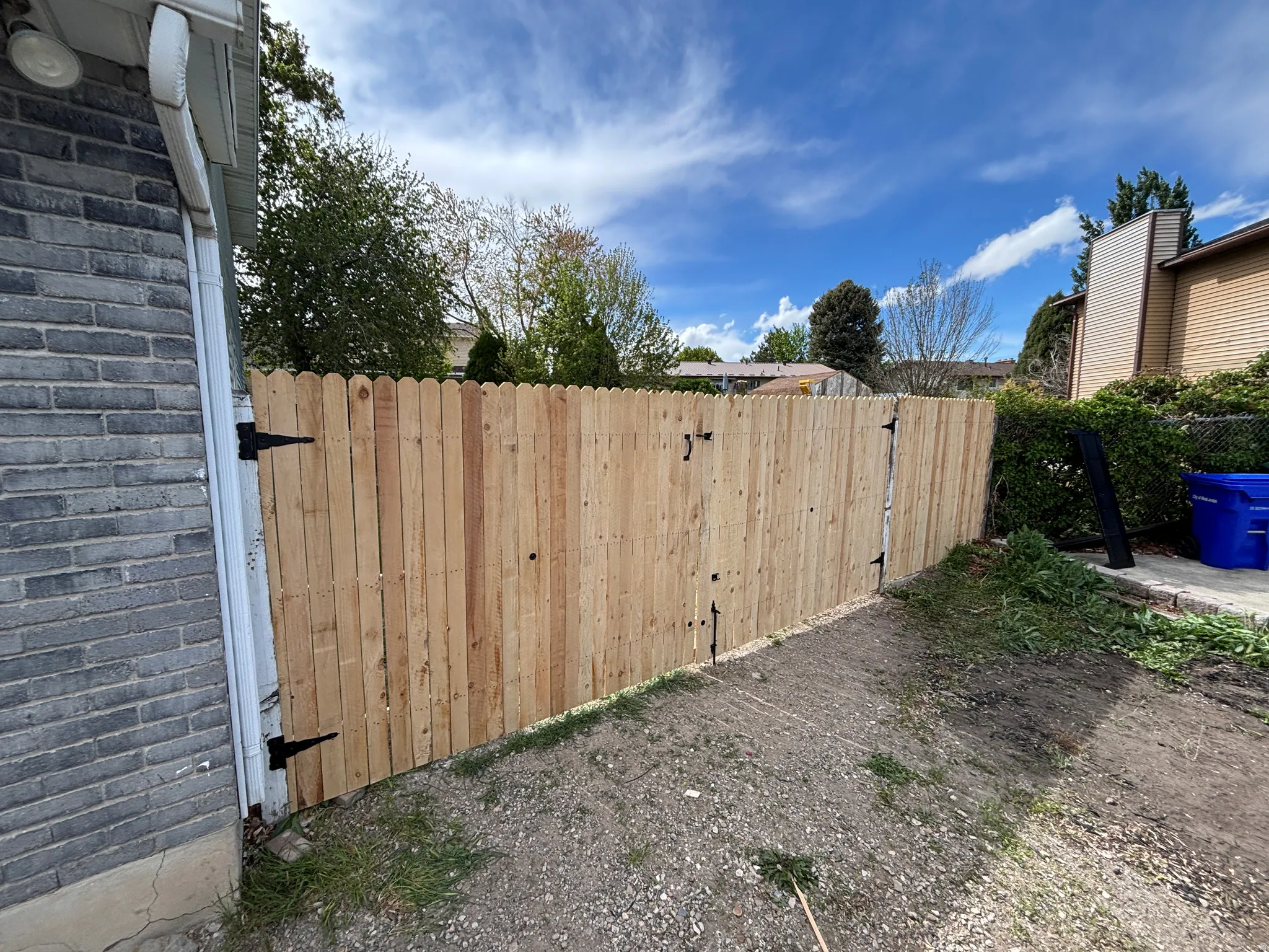 Wood privacy fence with two hinged gate sections, bordered by a gray brick exterior