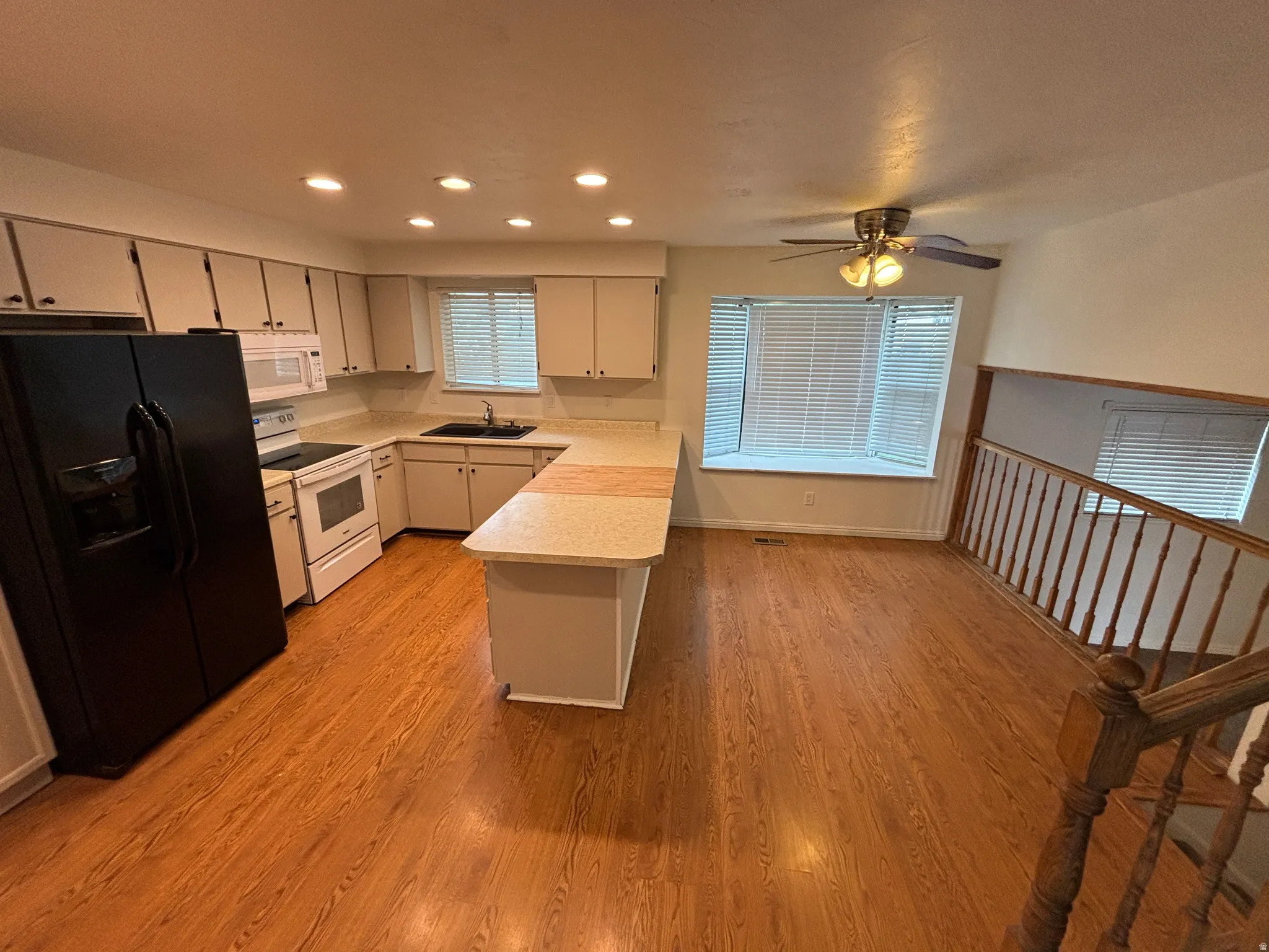 Kitchen and dining area featuring wood-finish flooring, white cabinetry, and a peninsula with a breakfast bar