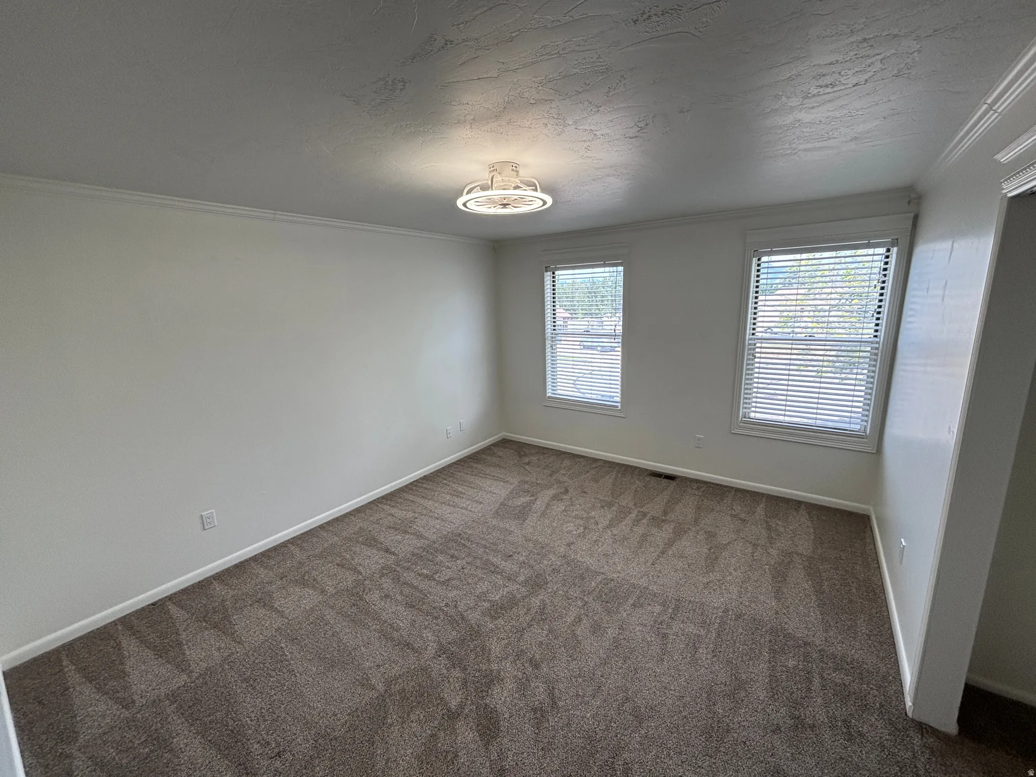 Carpeted room featuring two windows with horizontal blinds, white walls, and crown molding