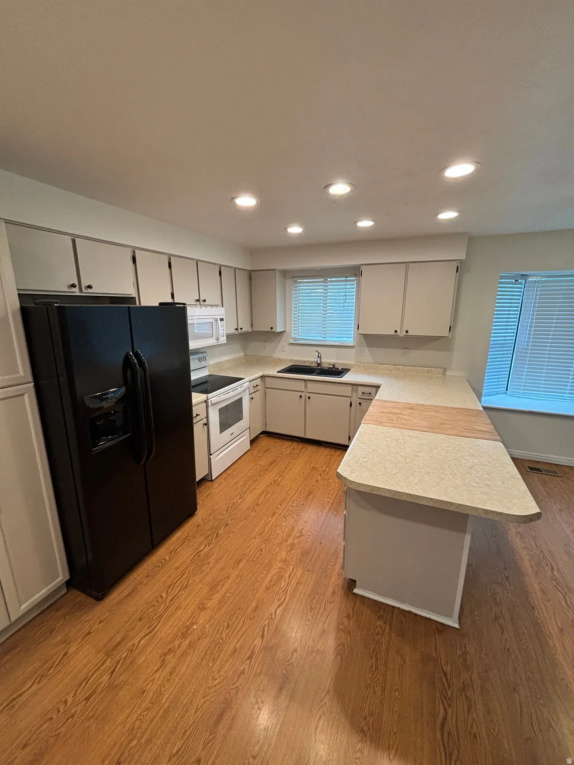 Kitchen featuring wood-finish flooring, white cabinetry, recessed lighting, white appliances, and a peninsula with a light-toned countertop