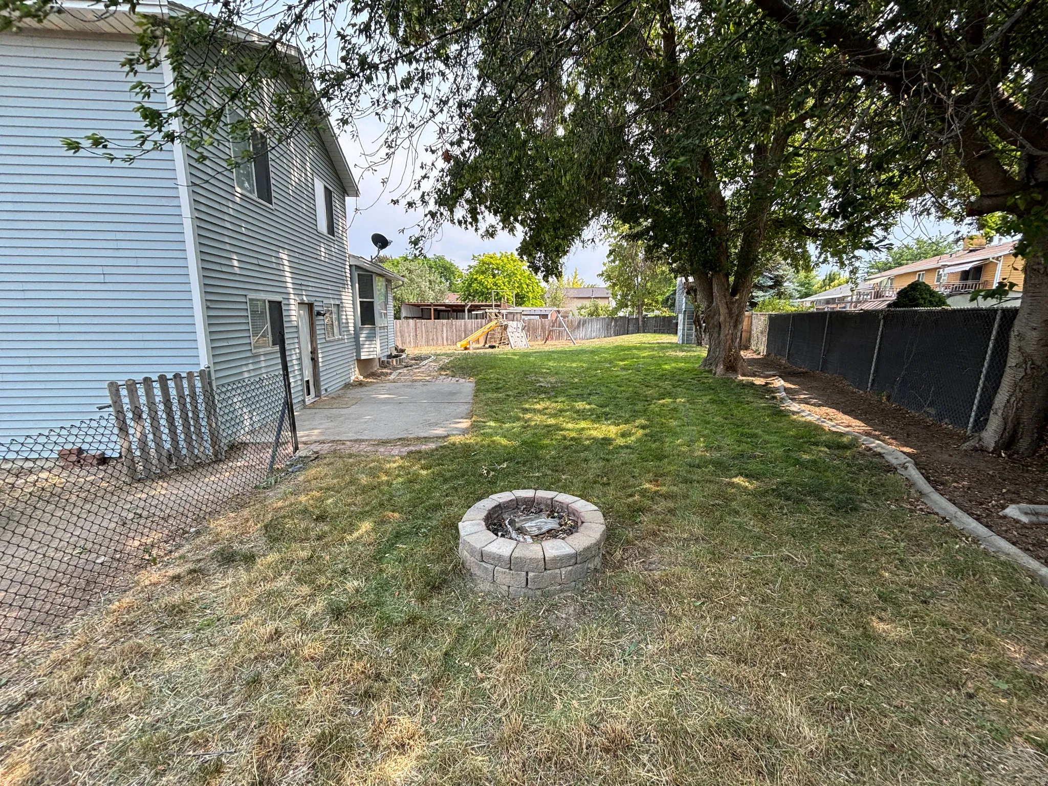 Expansive backyard featuring a stone-ringed fire pit, a concrete patio, and a chain-link fence