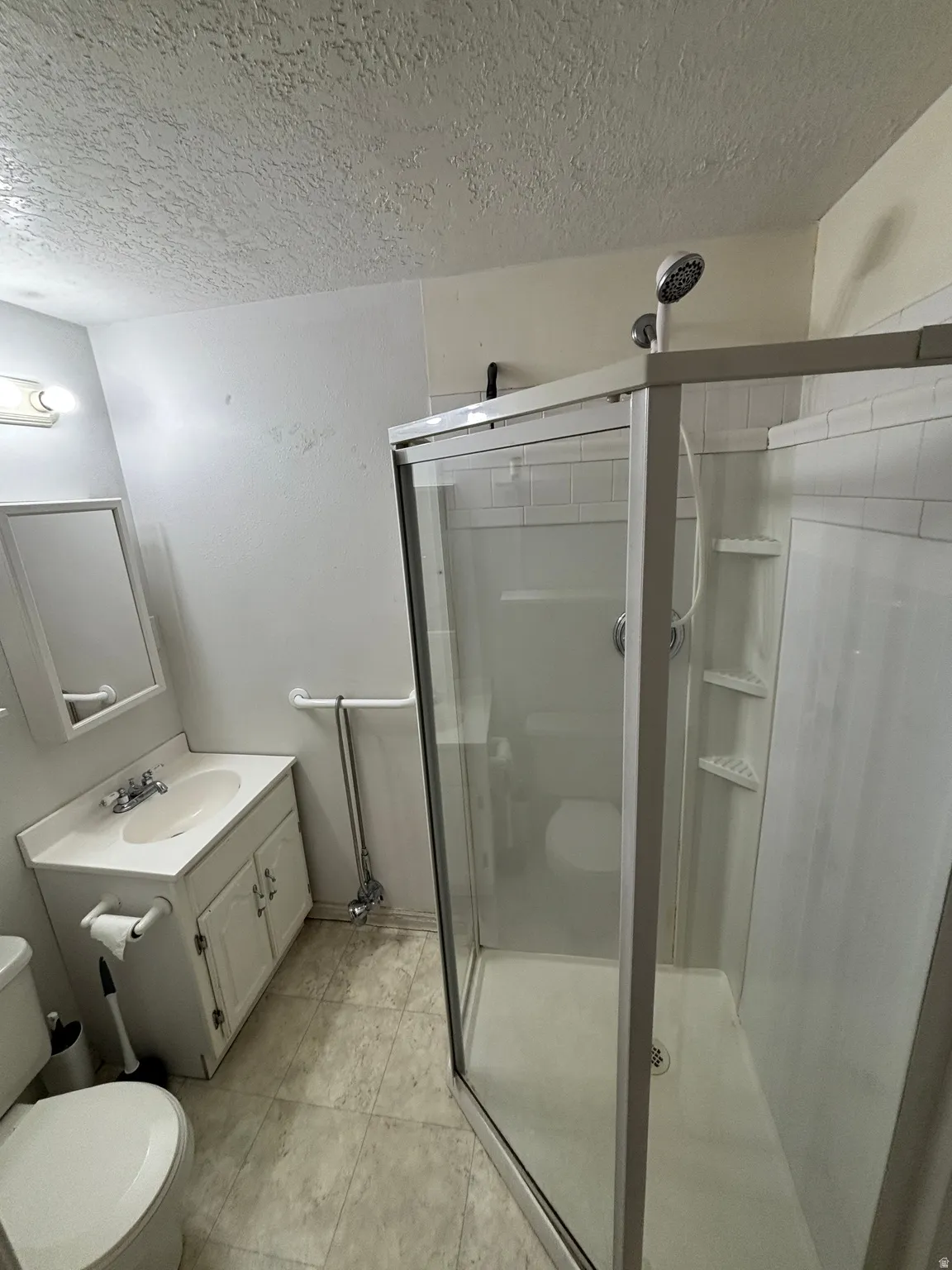 Bathroom featuring a clear glass shower enclosure, white vanity with integrated sink, wall-mounted mirror, and patterned flooring
