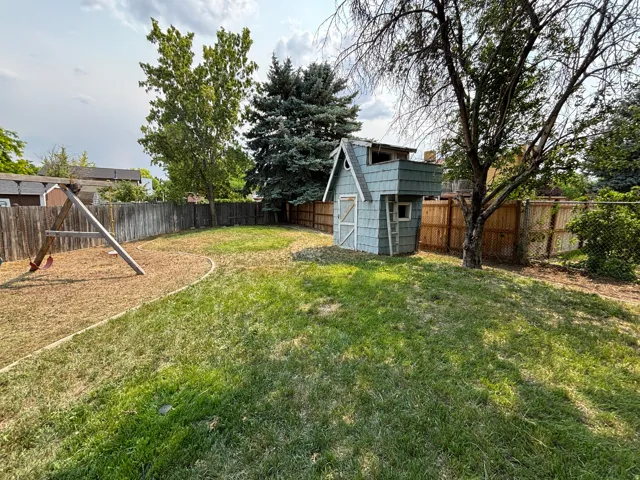 Spacious backyard featuring a wood privacy fence, established trees, and a dedicated play area with wood chip ground cover