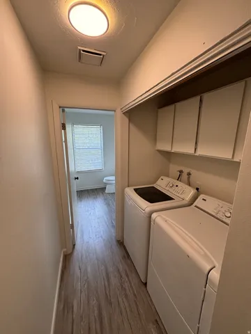 Dedicated laundry area featuring wood-finish flooring, white built-in cabinetry, and a ceiling-mounted light fixture