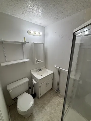 Bathroom featuring a white vanity with integrated sink, a toilet, and a glass-enclosed shower