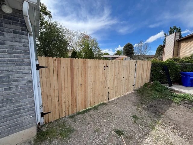 Wood privacy fence with two hinged gate sections, bordered by a gray brick exterior