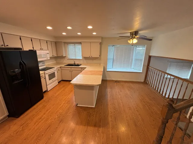 Kitchen and dining area featuring wood-finish flooring, white cabinetry, and a peninsula with a breakfast bar
