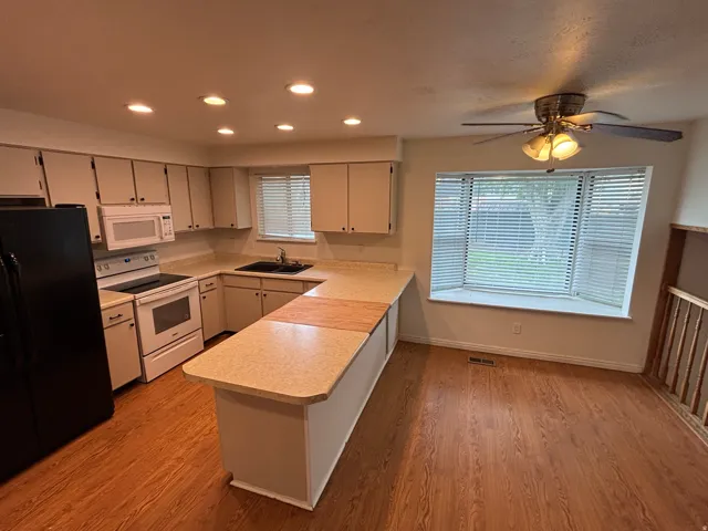Kitchen featuring wood-finish flooring, white cabinetry, a black refrigerator, white range, and built-in microwave