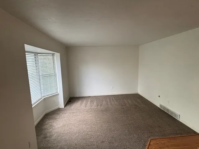 Bay window with horizontal blinds, neutral wall paint, and textured carpet flooring