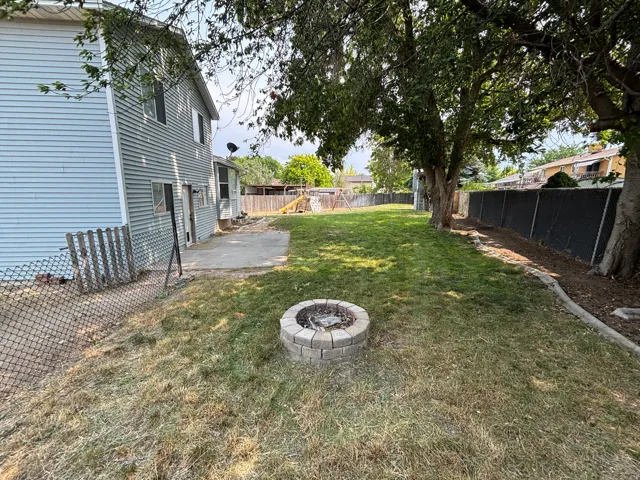 Expansive backyard featuring a stone-ringed fire pit, a concrete patio, and a chain-link fence