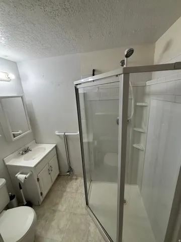 Bathroom featuring a clear glass shower enclosure, white vanity with integrated sink, wall-mounted mirror, and patterned flooring