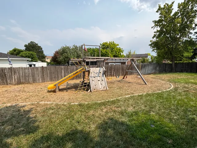 Expansive backyard featuring a wood privacy fence, a dedicated play area with a playground structure, and a combination of natural grass and wood chip ground cover