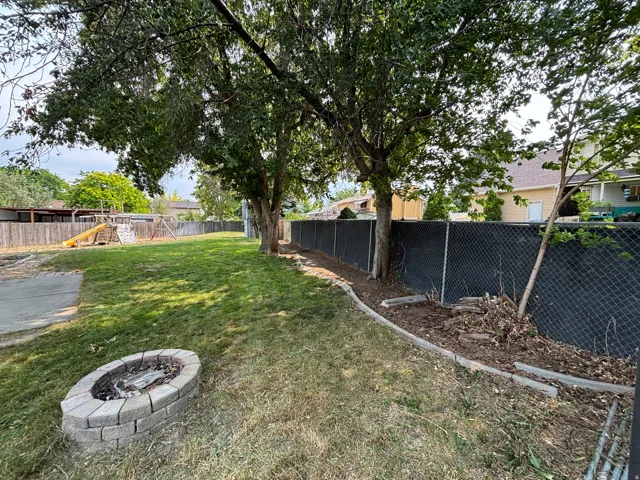 Expansive backyard featuring a stone-lined fire pit, mature trees, and a chain-link fence