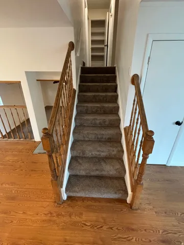 Carpeted staircase with wood banister and balusters