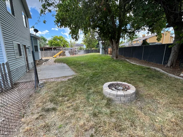 Expansive backyard featuring a stone block fire pit, mature trees, and a concrete patio pad