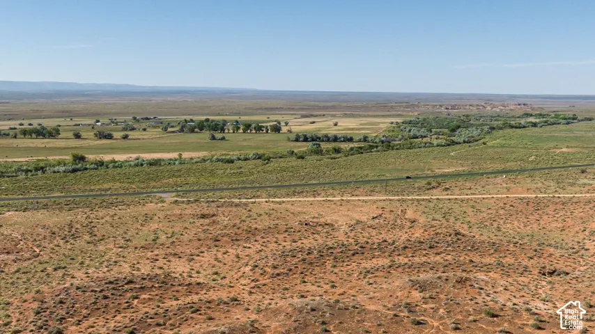Expansive desert landscape featuring a paved road, a secondary unpaved road, and distant green foliage