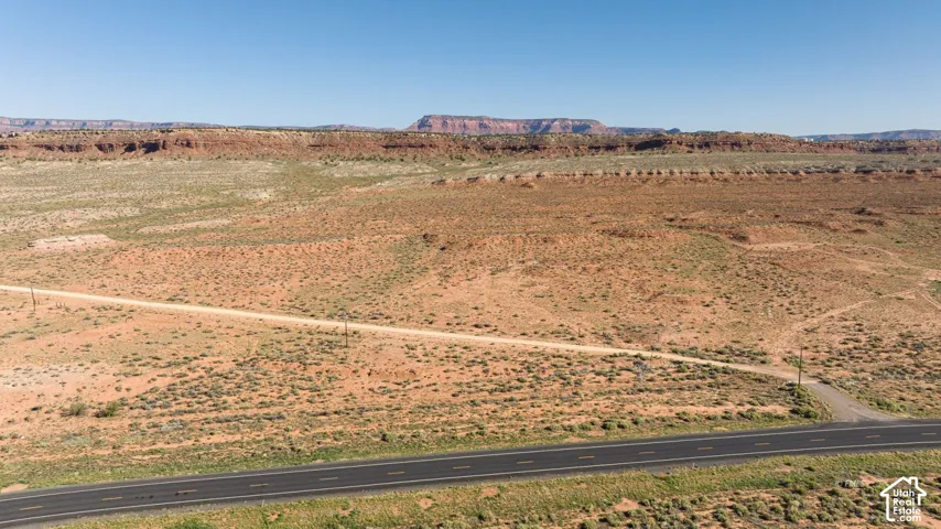 Expansive undeveloped land featuring a paved road frontage, a visible dirt road entrance, and a clear desert landscape