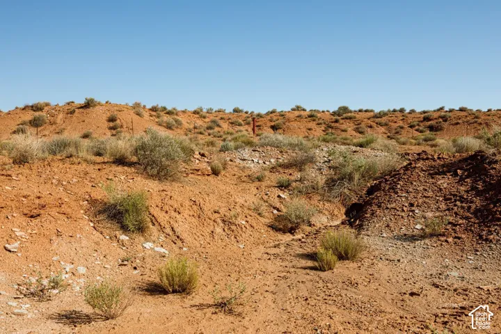 Expansive desert landscape featuring rolling hills and sparse shrubbery under a clear blue sky