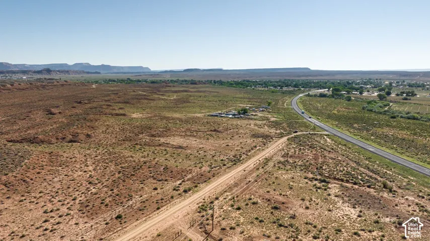 Expansive undeveloped land featuring a dirt road, paved highway, and distant rock formations