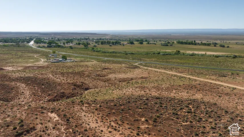 Expansive desert landscape featuring a clear sky, distant paved road, and scattered structures