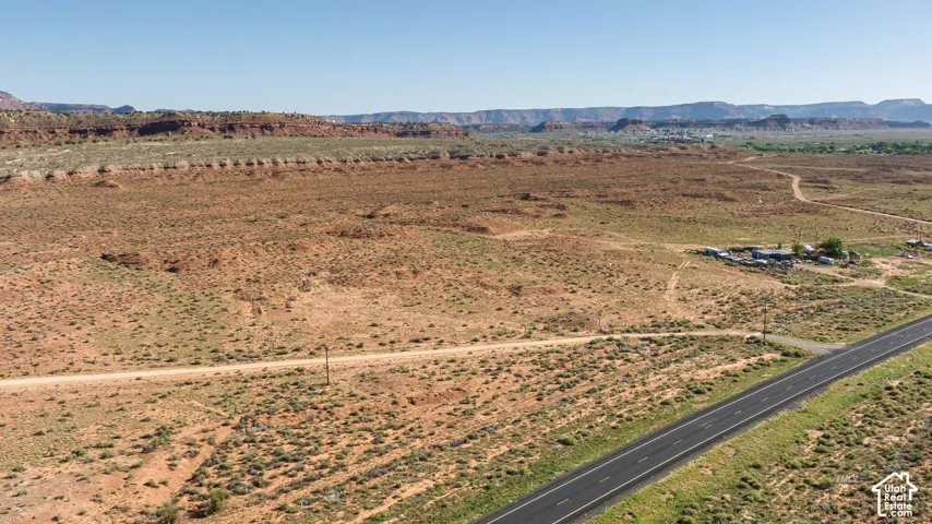 Expansive desert landscape featuring a paved road, dirt paths, and distant mountain formations under a clear sky