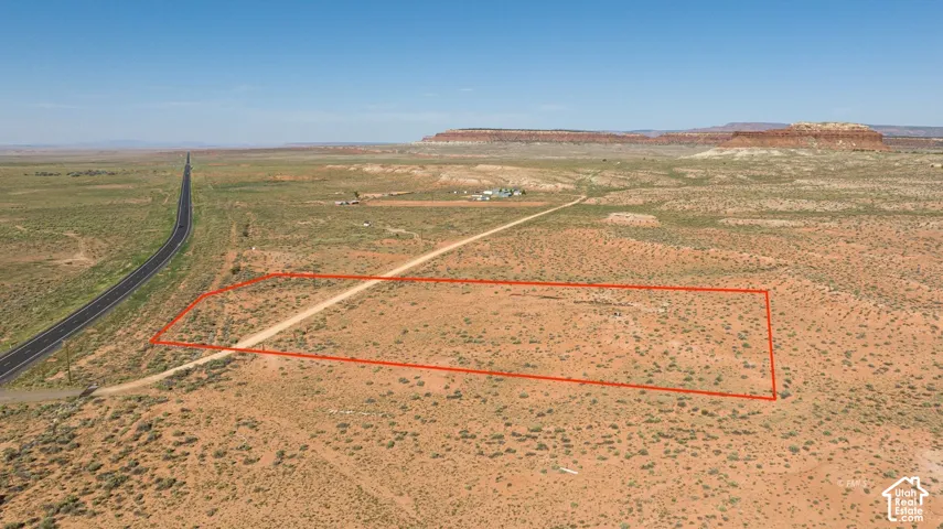 Expansive desert land featuring a paved road, a dirt road, and distant mesa formations