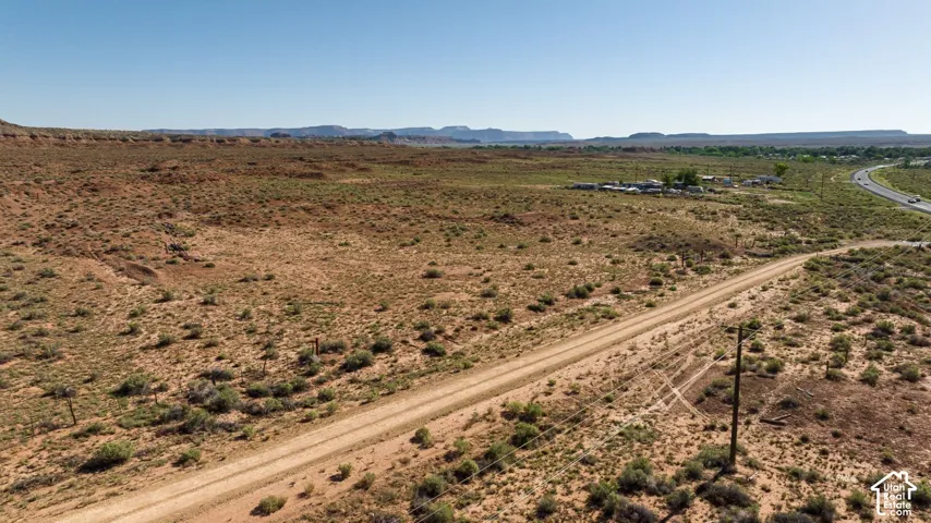 Expansive desert landscape featuring a dirt road, sparse vegetation, and distant highway access