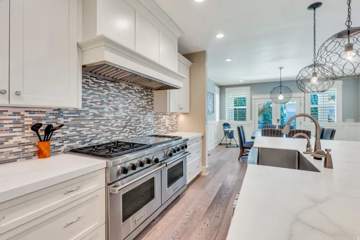 Gourmet kitchen featuring a professional-grade range, tiled backsplash, white cabinetry, and wood-finish flooring