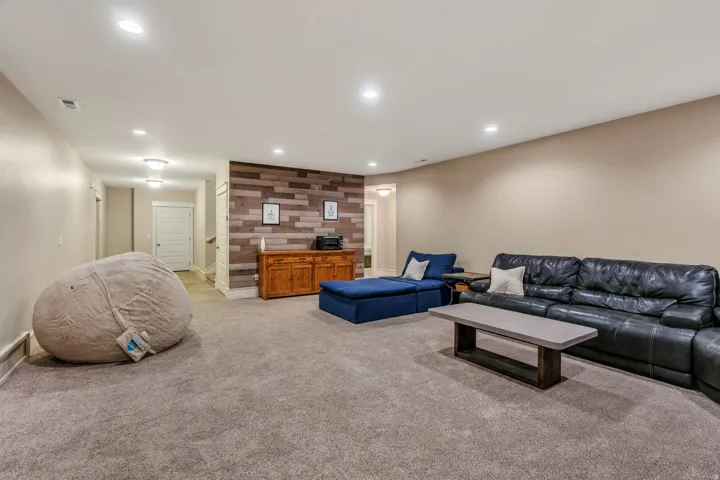 Spacious recreation room featuring recessed lighting, plush carpeting, a wood-paneled accent wall, and a built-in wooden console